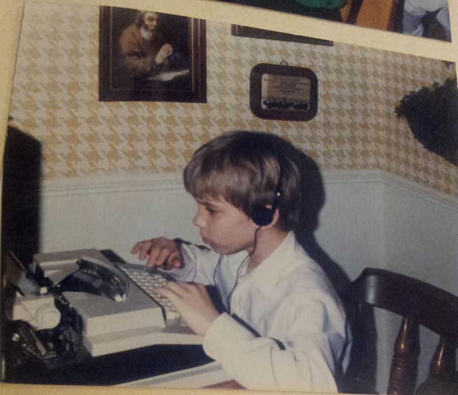 A young child in headphones typing at a typewriter