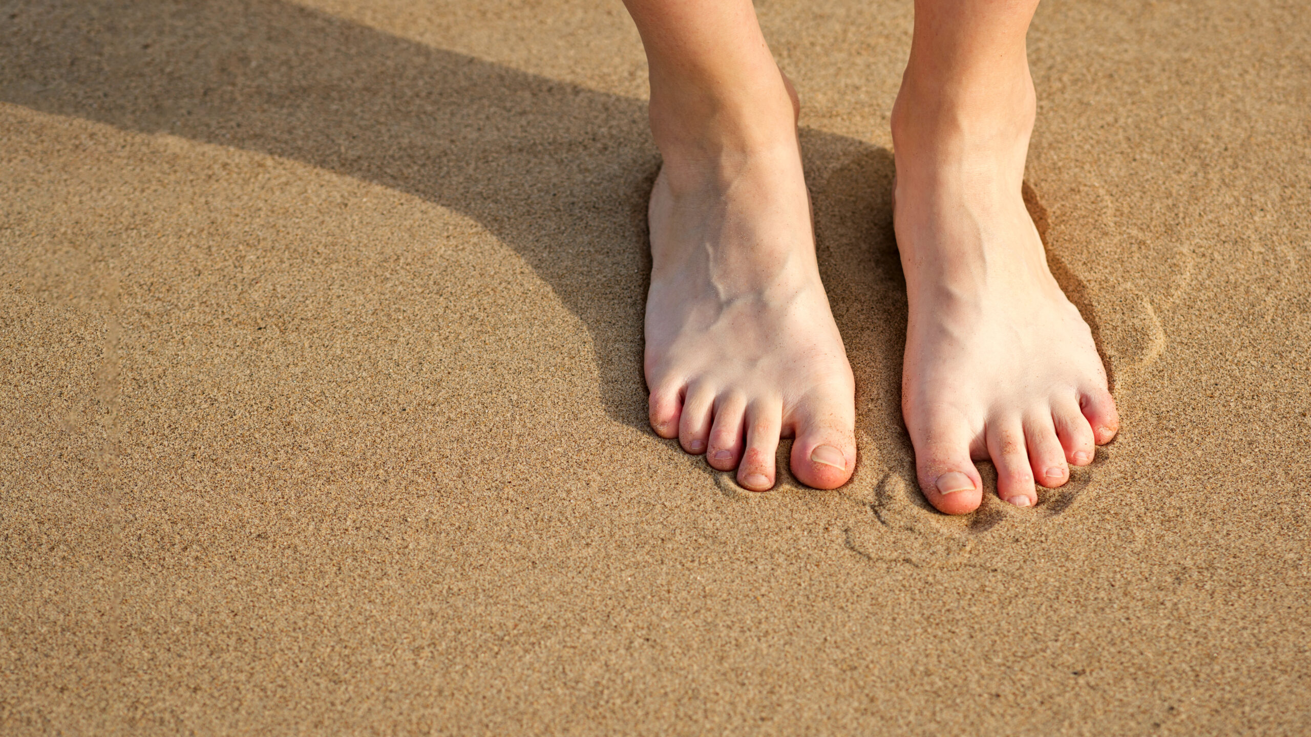 Close-up female legs with uneven tans on sand. Feet girl on sandy beach.